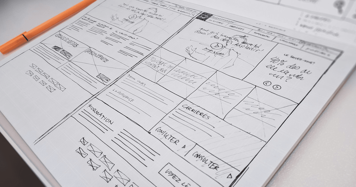 Website wireframe sketched in a notebook next to a laptop and coffee
